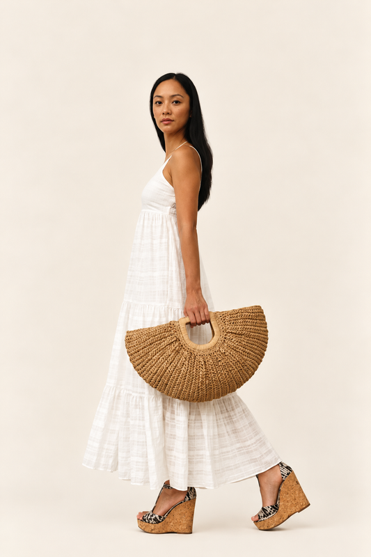 Model carrying Lua woven straw bag with a white summer dress and sandals
