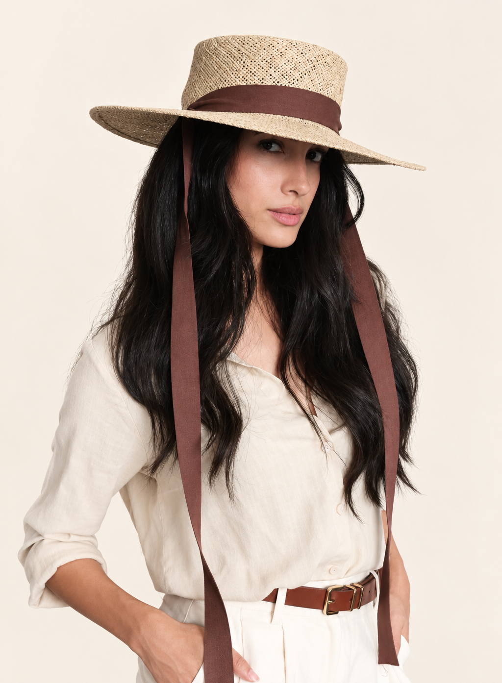 Model wearing Elise Straw Boater Hat with brown ribbon, styled with a beige blouse and shorts